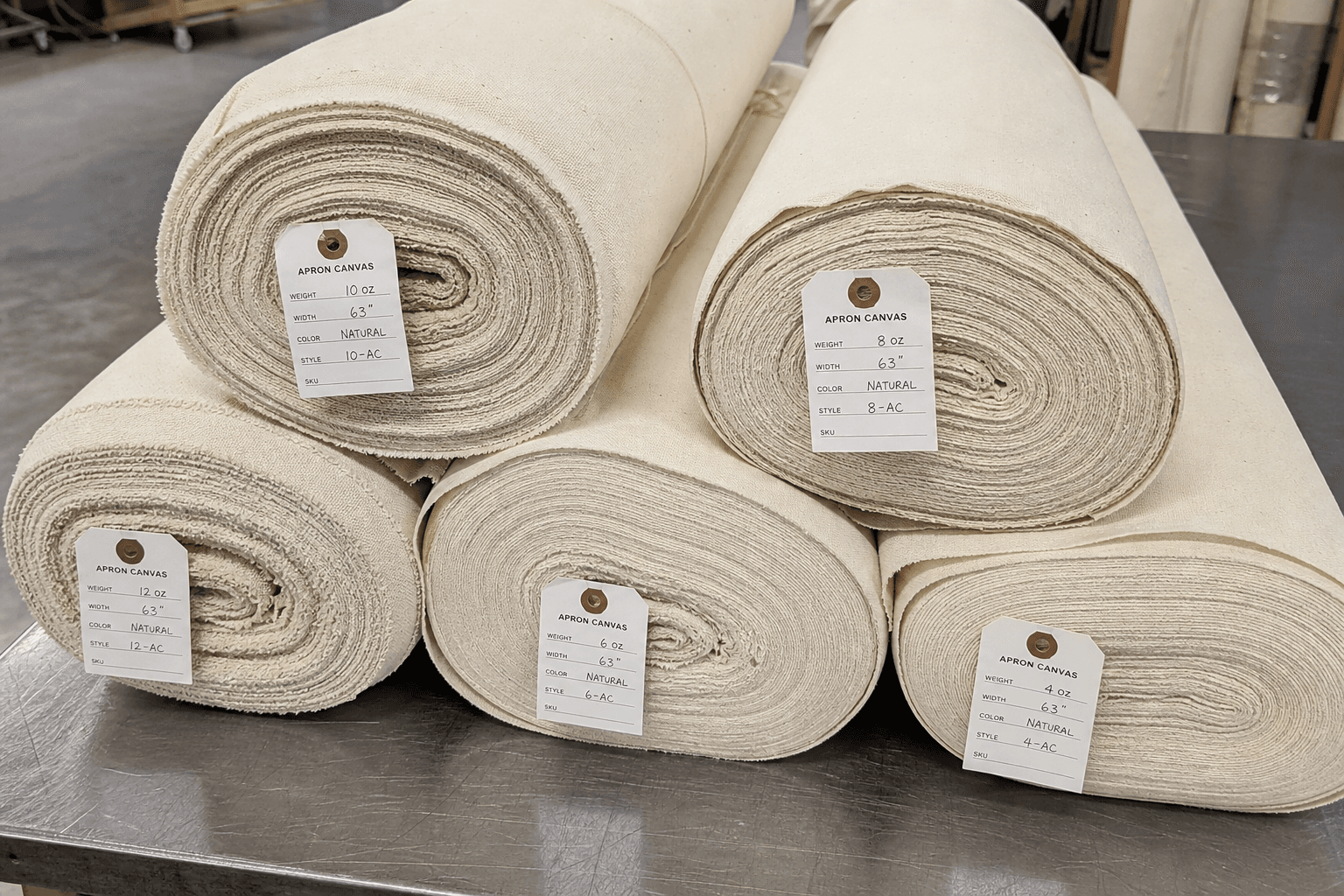 Stacked cotton canvas apron fabric rolls in graded weights on a factory table